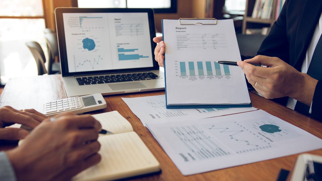 Laptop analytics dashboard alongside analytics documents with two individuals writing notes | hotel channel manager 